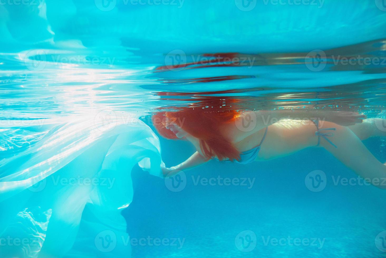 Portrait of smiling young beautiful red-haired girl in sunny day in open swimming pool in summer underwater photo