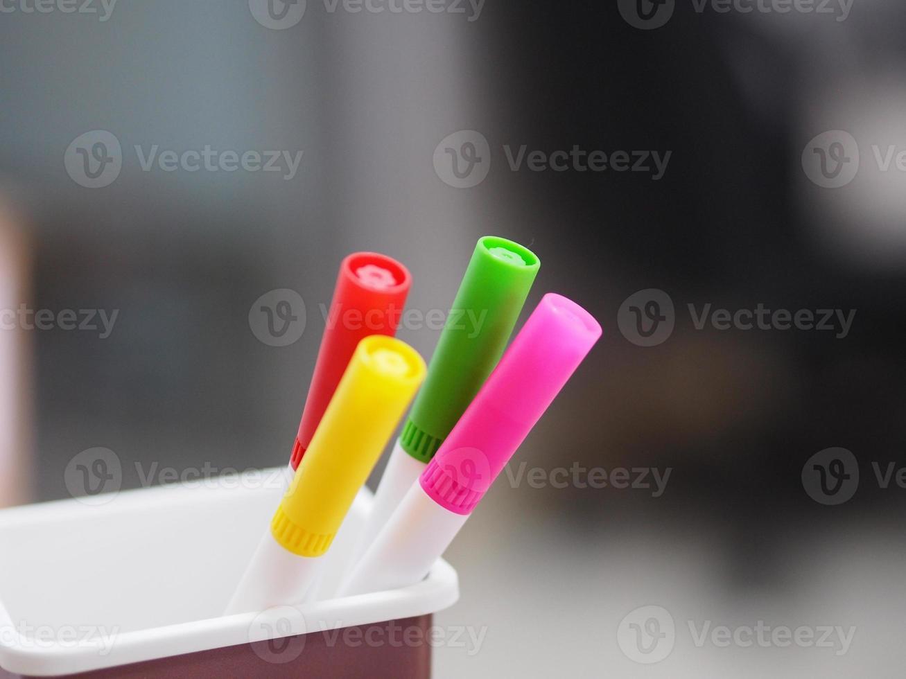 many magic pen red, pink, yellow, green color in brown plastic box, blurred of notebook background photo