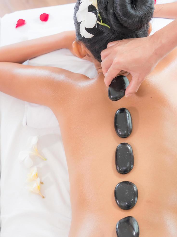 A beautiful Asian woman is relaxing in a spa shop when an expert masseuse places a hot stone on her back photo