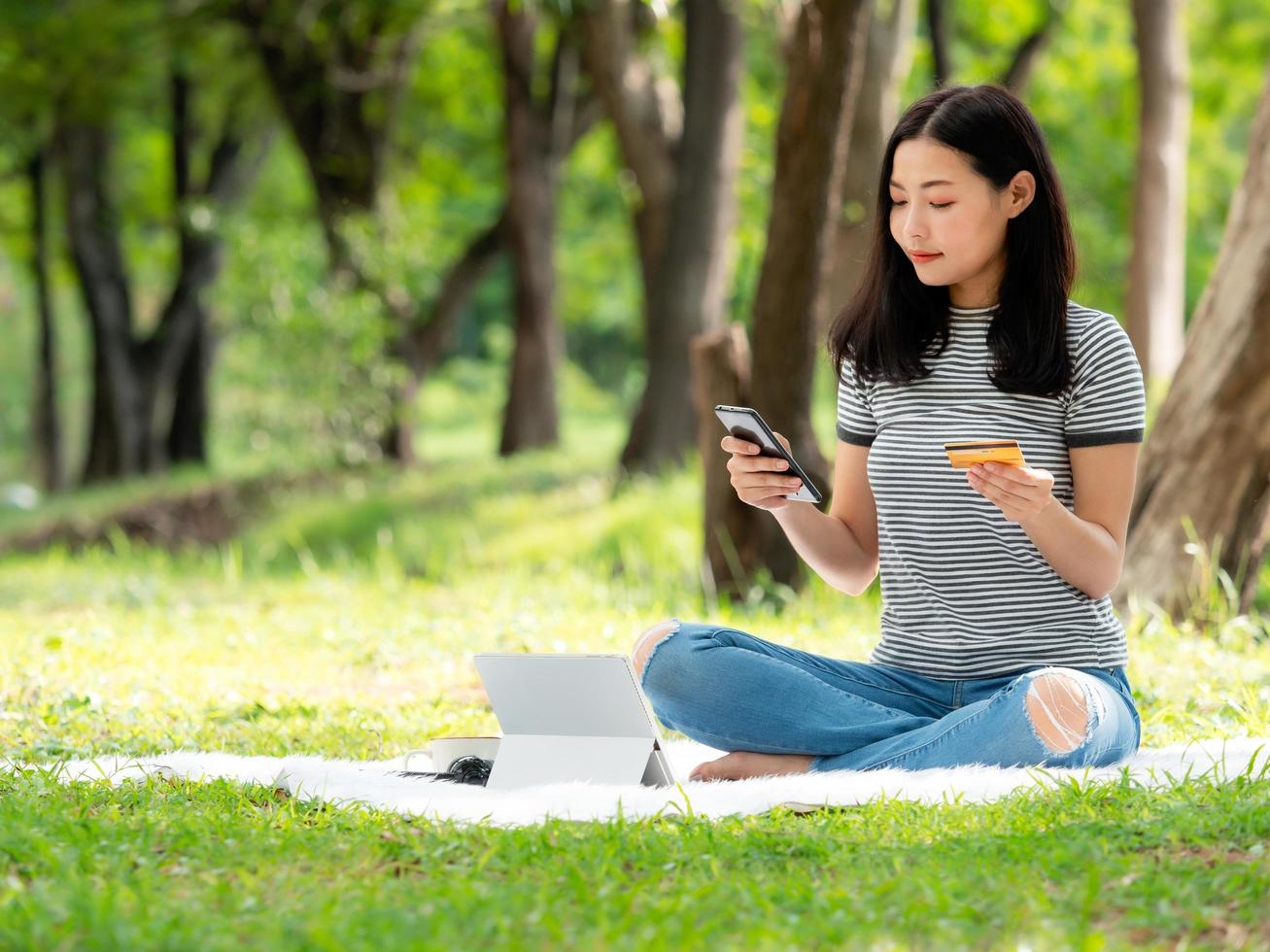 A beautiful Asian woman is happy as she uses her credit card to make purchases online via smartphone photo