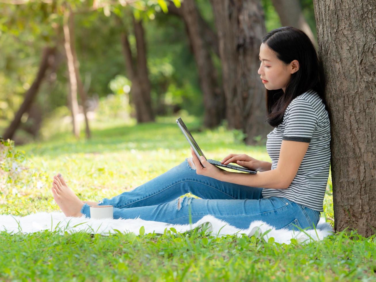una hermosa mujer asiática se relaja en el jardín, lee y busca información de aprendizaje en Internet foto