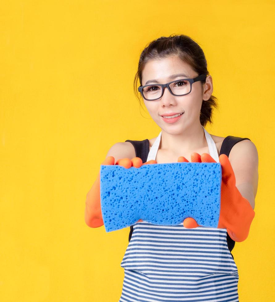 hermosa mujer asiática sosteniendo una esponja para limpiar el dispositivo y sonriendo alegremente para limpiar la casa foto