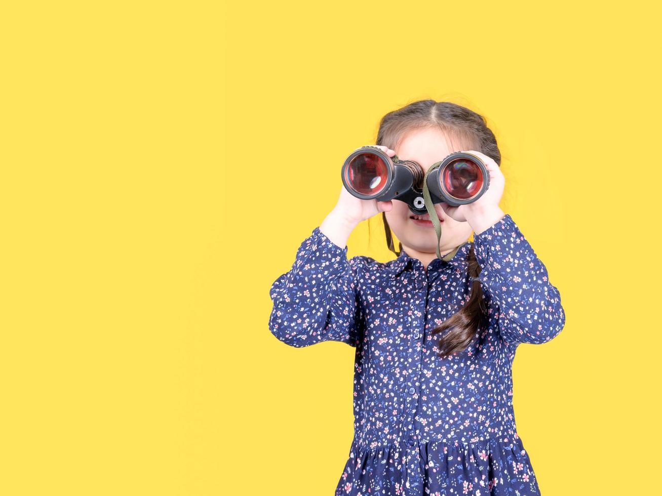 A cute girl raises a binoculars to look at the outside world through the lens photo