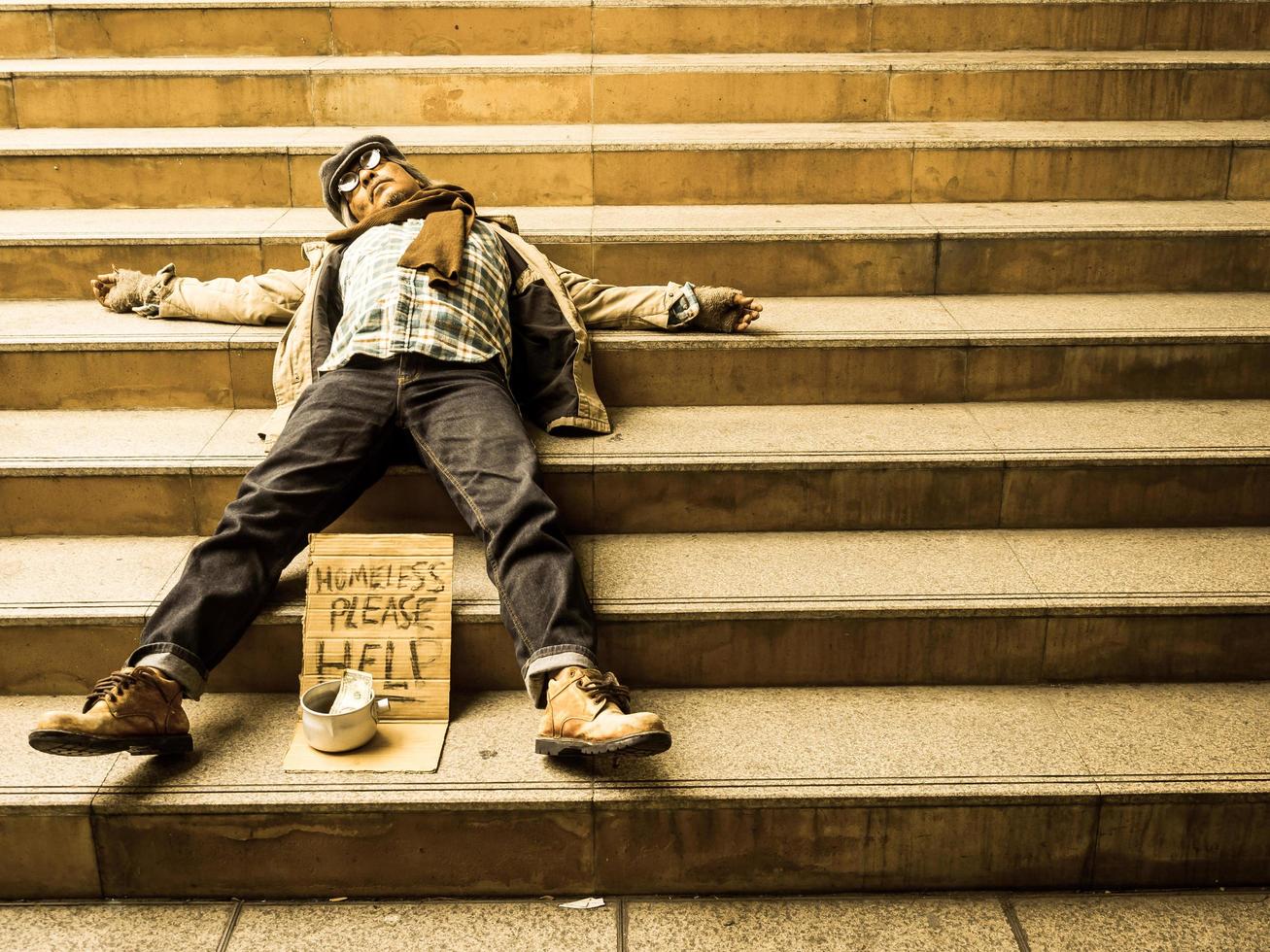 A poor homeless man sleep on a ladder with a donation bill photo
