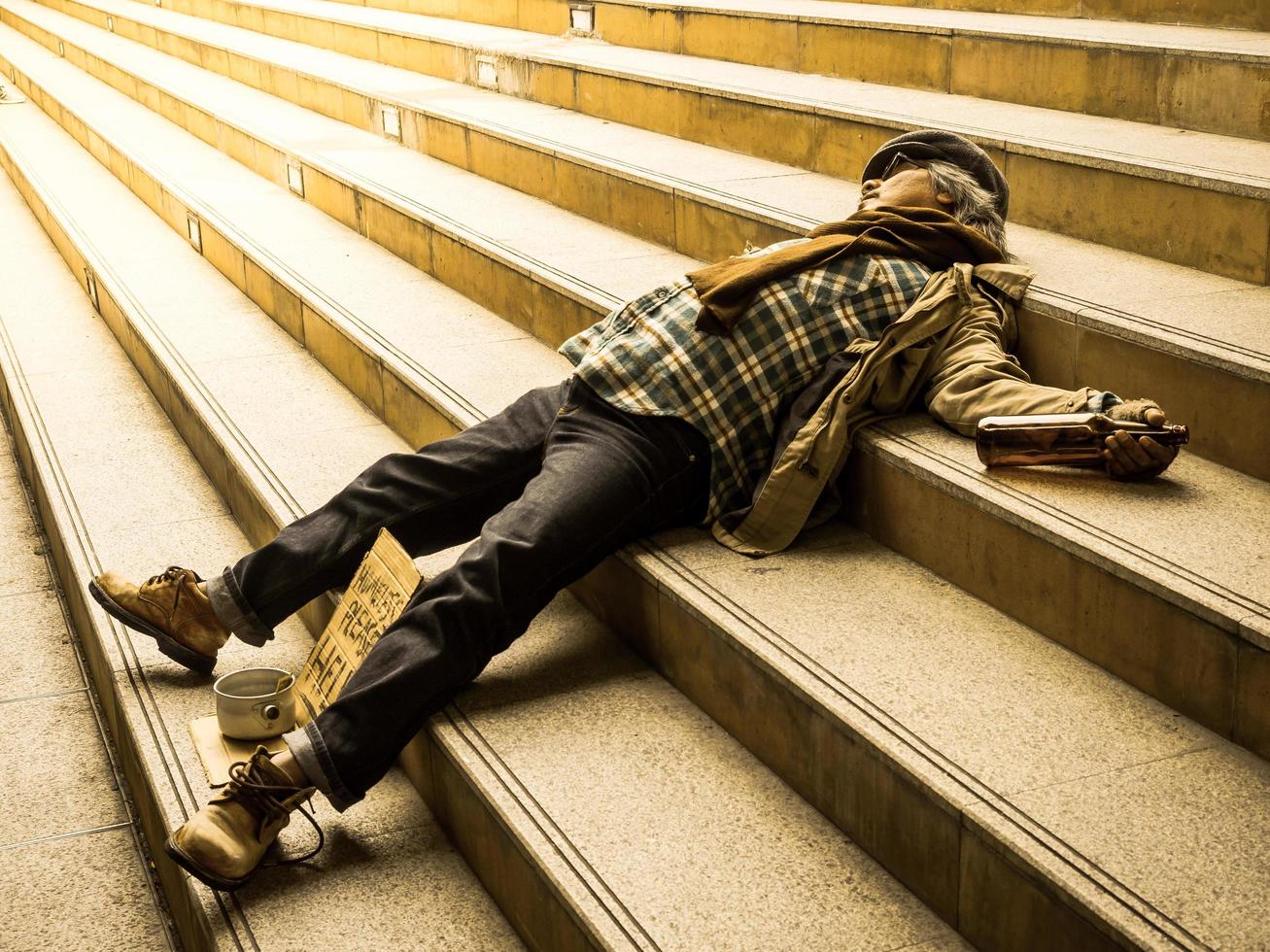 un pobre hombre sin hogar duerme en una escalera con una factura de donación foto