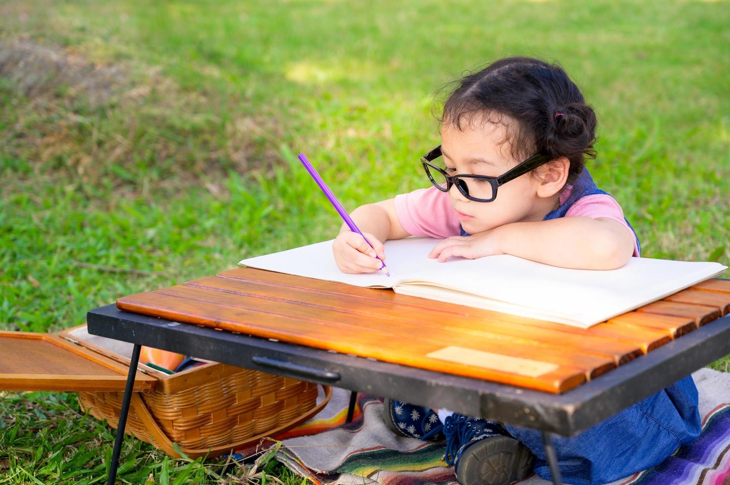 A little girl is sitting on the cloth and painted on the paper placed on a table photo