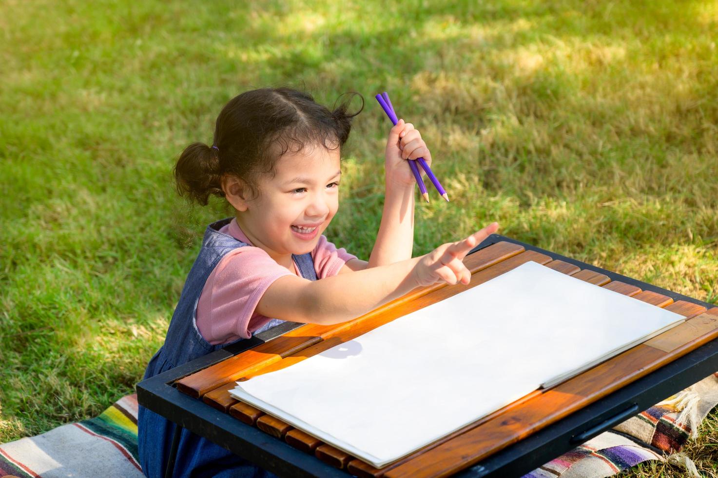 A little girl is sitting on the cloth and painted on the paper placed on a table photo