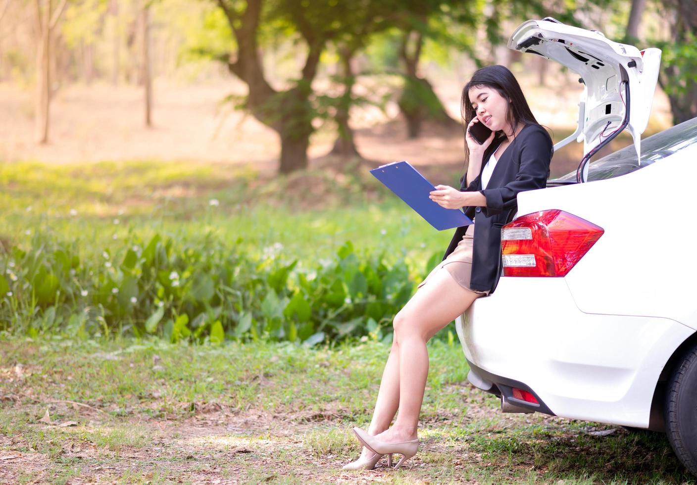 una hermosa mujer asiática sentada en la parte trasera de un auto y usando un teléfono móvil para trabajar fuera de la oficina. el concepto de trabajar en casa durante la epidemia del virus de la corona foto