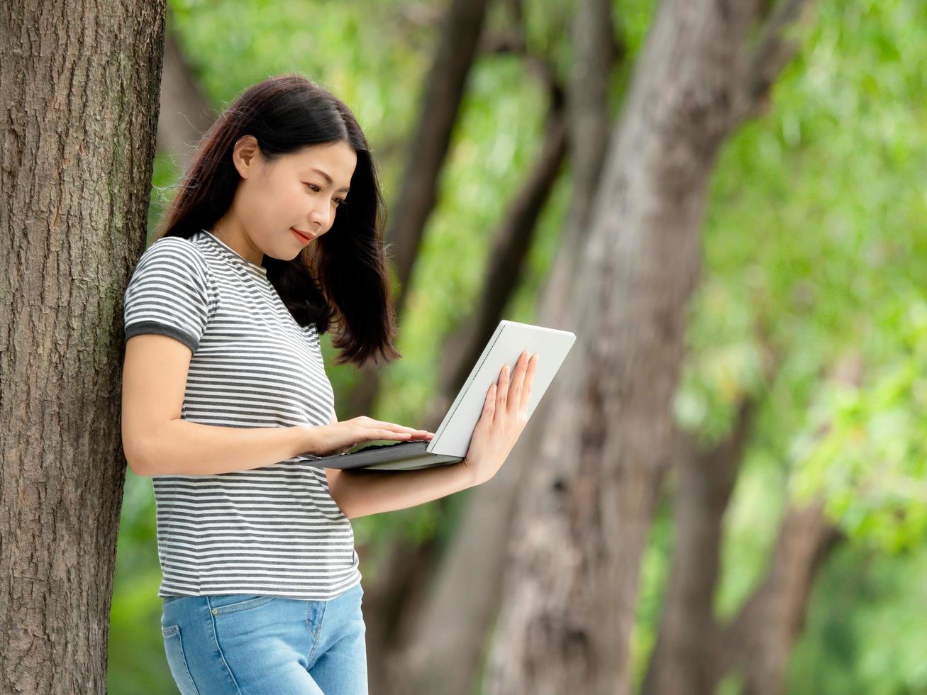 una hermosa mujer asiática se relaja en el jardín, lee y busca información de aprendizaje en Internet foto