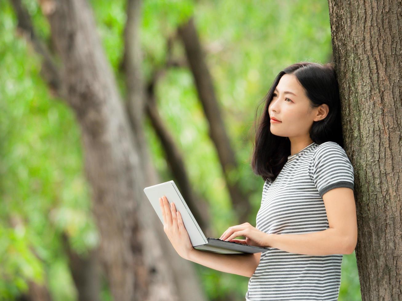 una hermosa mujer asiática se relaja en el jardín, lee y busca información de aprendizaje en Internet foto