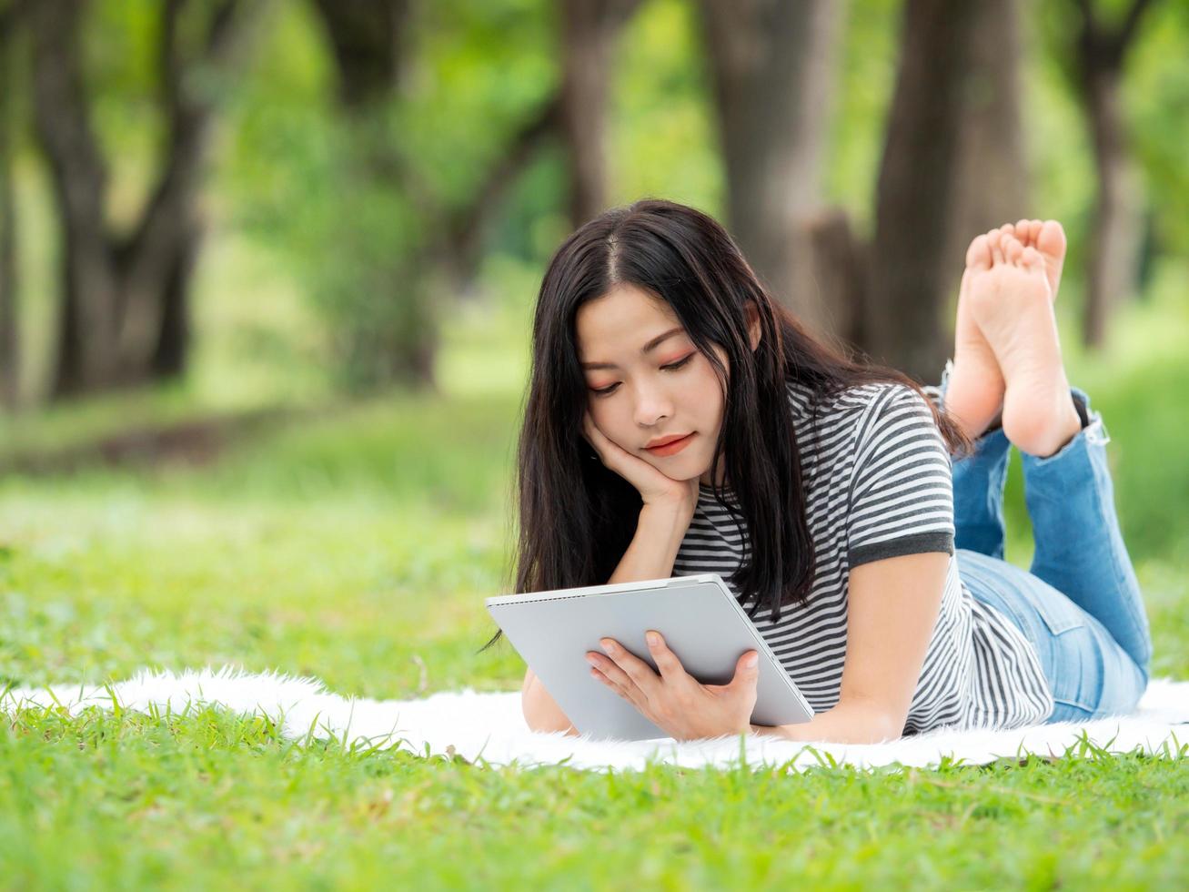 una hermosa mujer asiática se relaja en el jardín, lee y busca información de aprendizaje en Internet foto