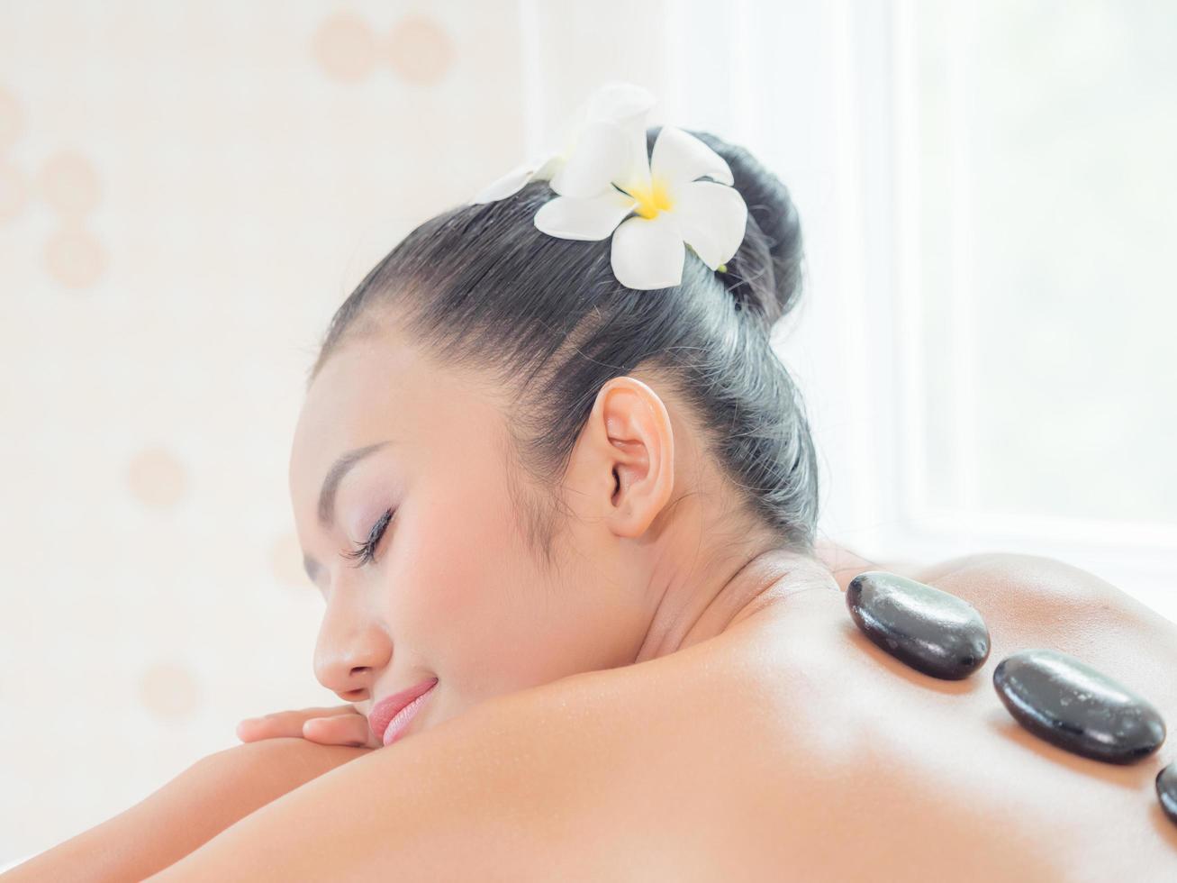 A beautiful Asian woman is relaxing in a spa shop when an expert masseuse places a hot stone on her back photo