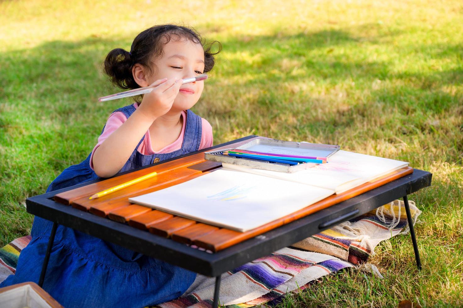 A little girl is sitting on the cloth and painted on the paper placed on a table photo