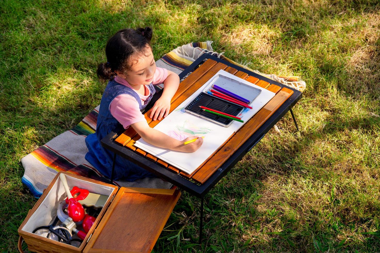 A little girl is sitting on the cloth and painted on the paper placed on a table photo