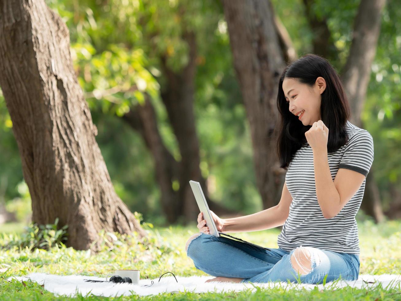 una hermosa mujer asiática está sentada en el jardín y está feliz después de buscar información en Internet foto