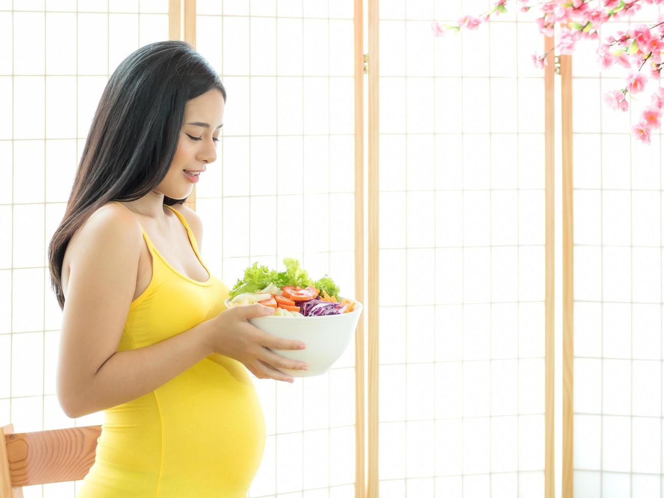 A beautiful pregnant woman in a Japanese room preparing a vegetable salad to eat for good health photo