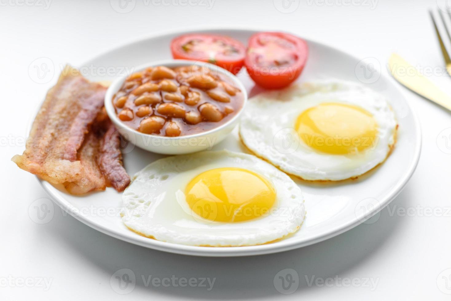 English breakfast with fried eggs, bacon, beans, tomatoes, spices and herbs photo