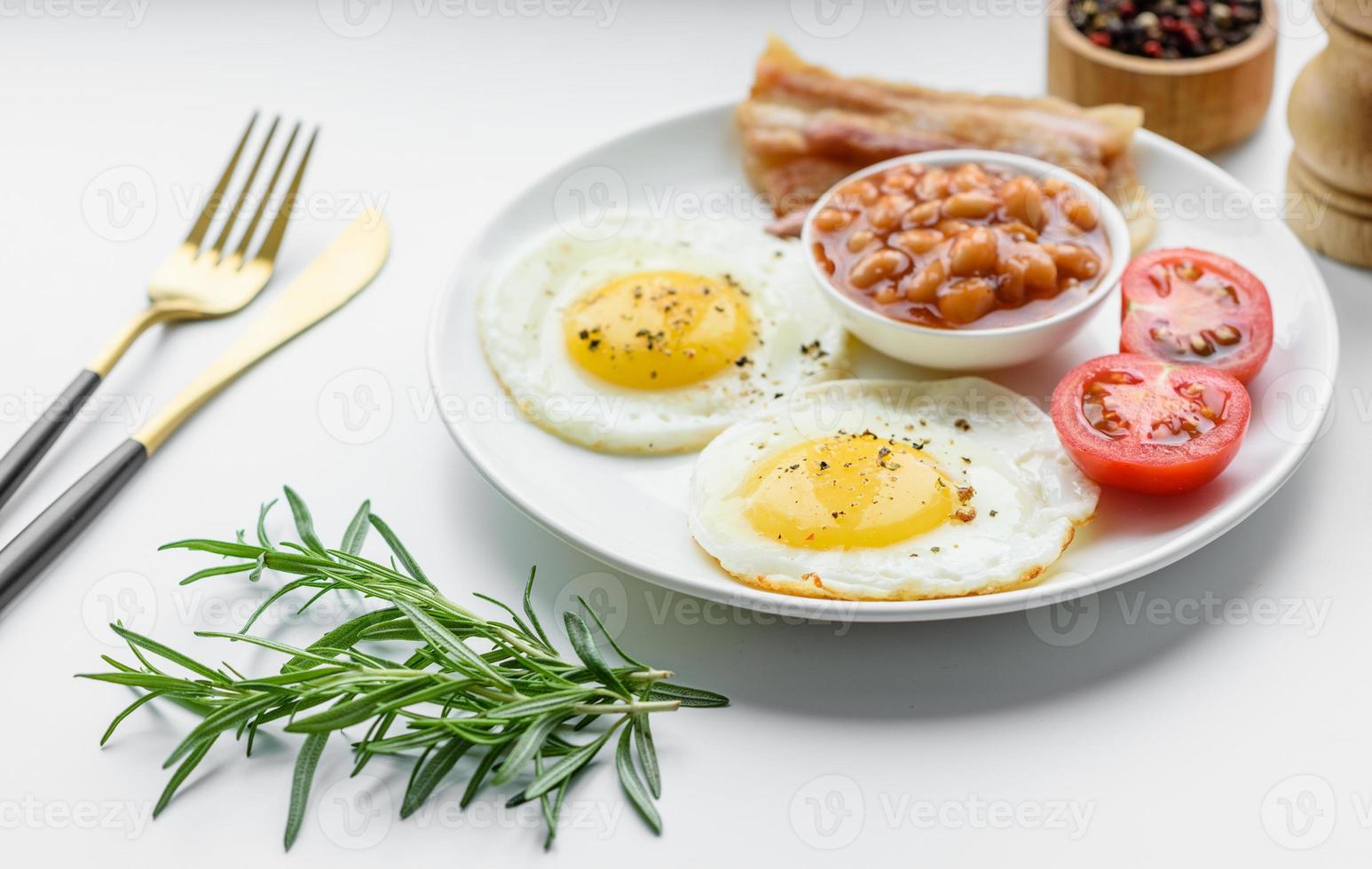 desayuno inglés con huevos fritos, tocino, frijoles, tomates, especias y hierbas foto