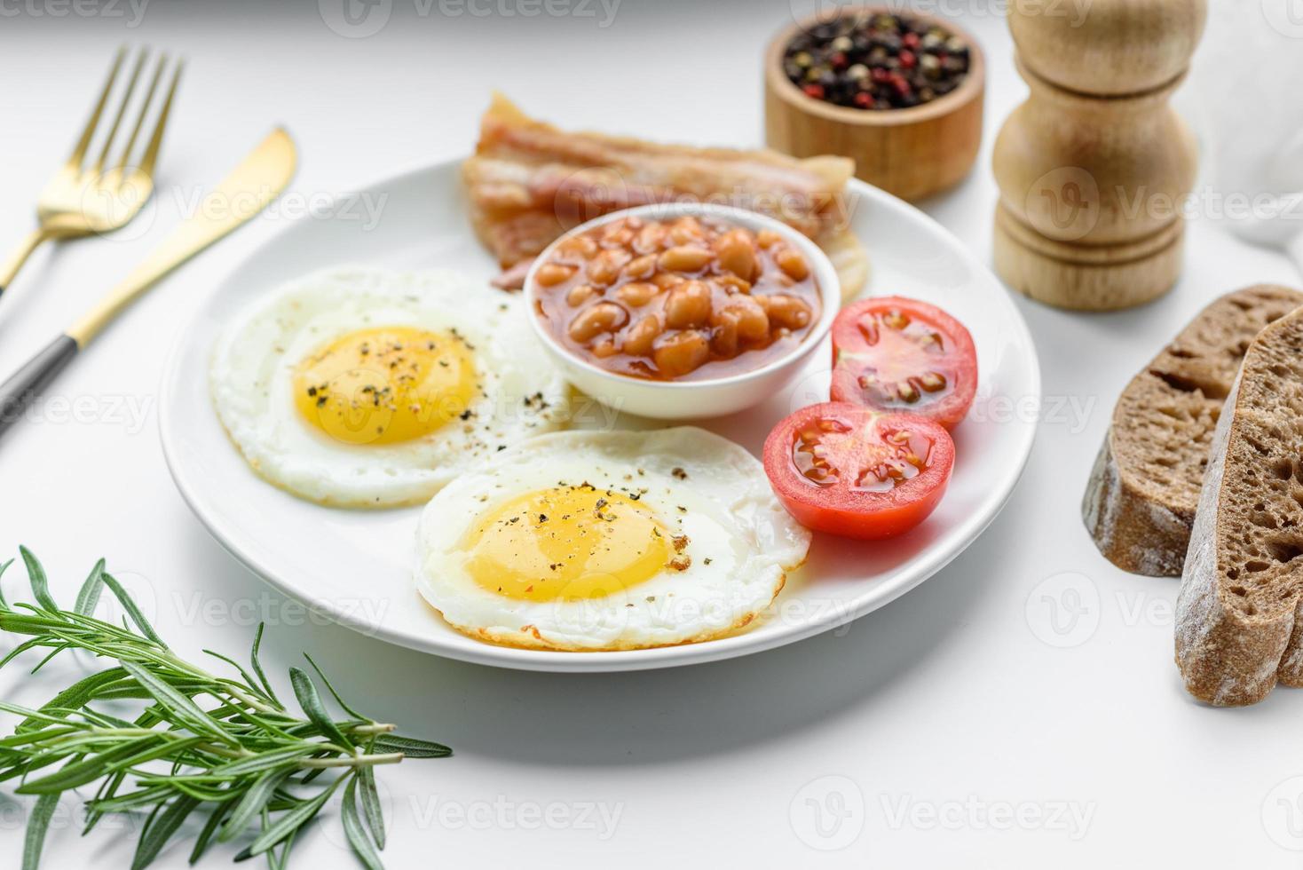 desayuno inglés con huevos fritos, tocino, frijoles, tomates, especias y hierbas foto