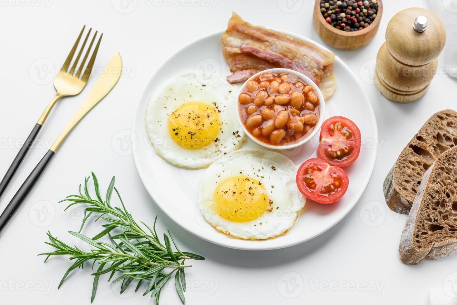 desayuno inglés con huevos fritos, tocino, frijoles, tomates, especias y hierbas foto