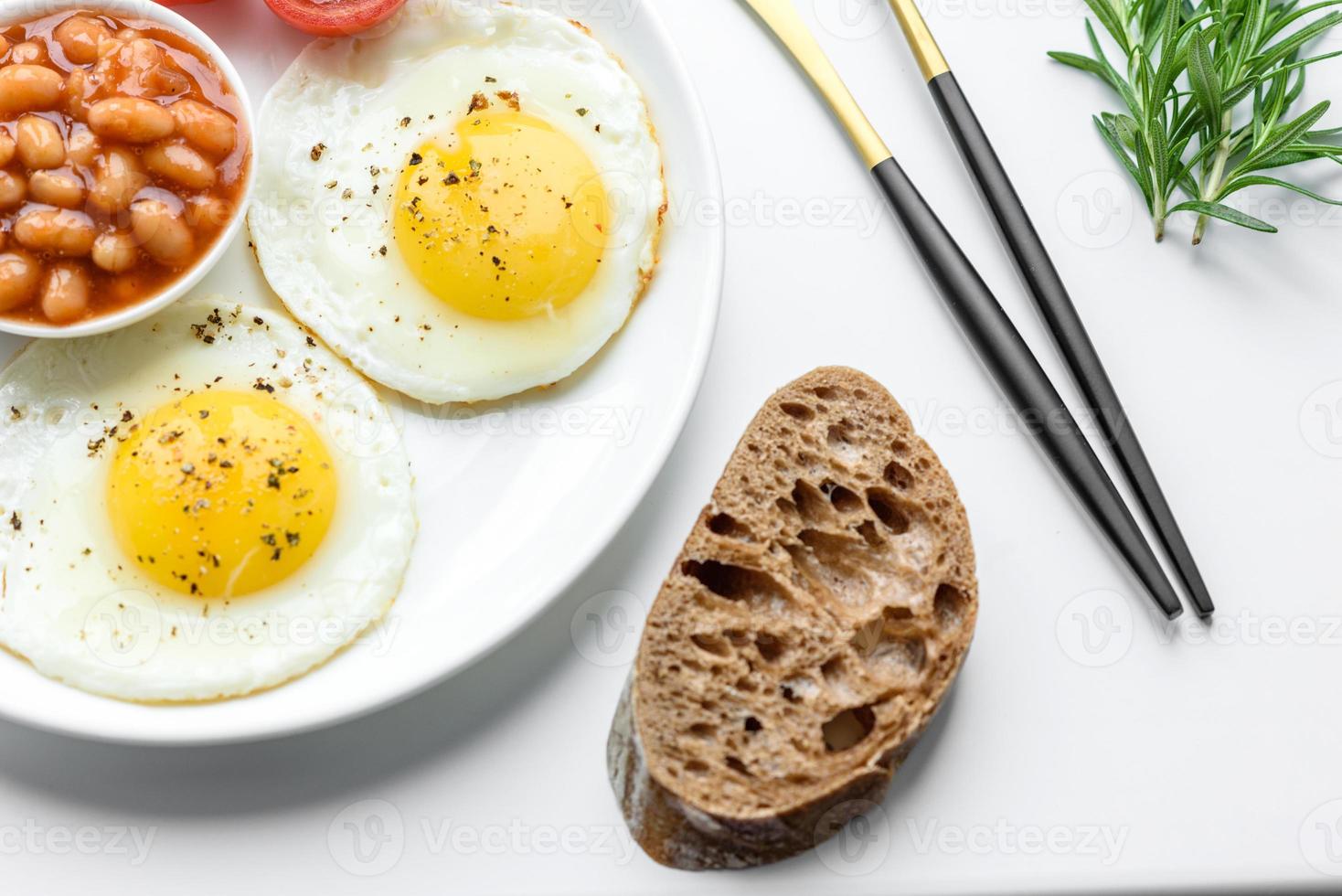 desayuno inglés con huevos fritos, tocino, frijoles, tomates, especias y hierbas foto