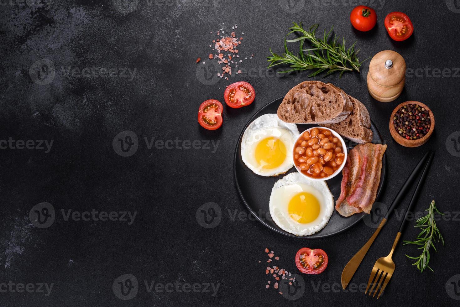 English breakfast with fried eggs, bacon, beans, tomatoes, spices and herbs photo