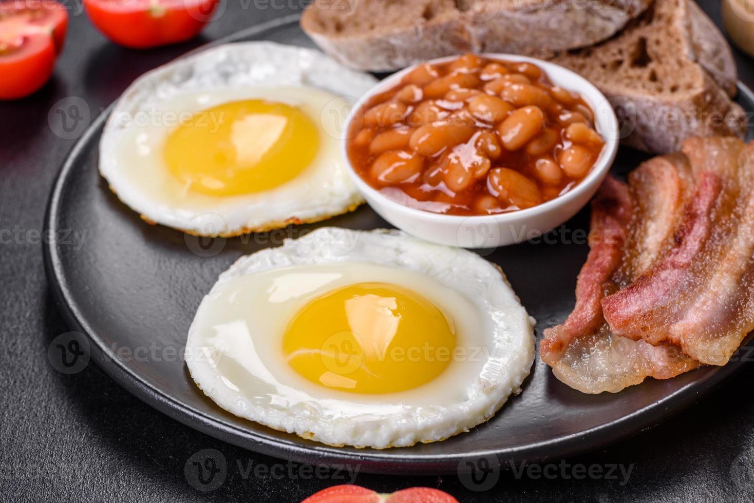 English breakfast with fried eggs, bacon, beans, tomatoes, spices and herbs photo