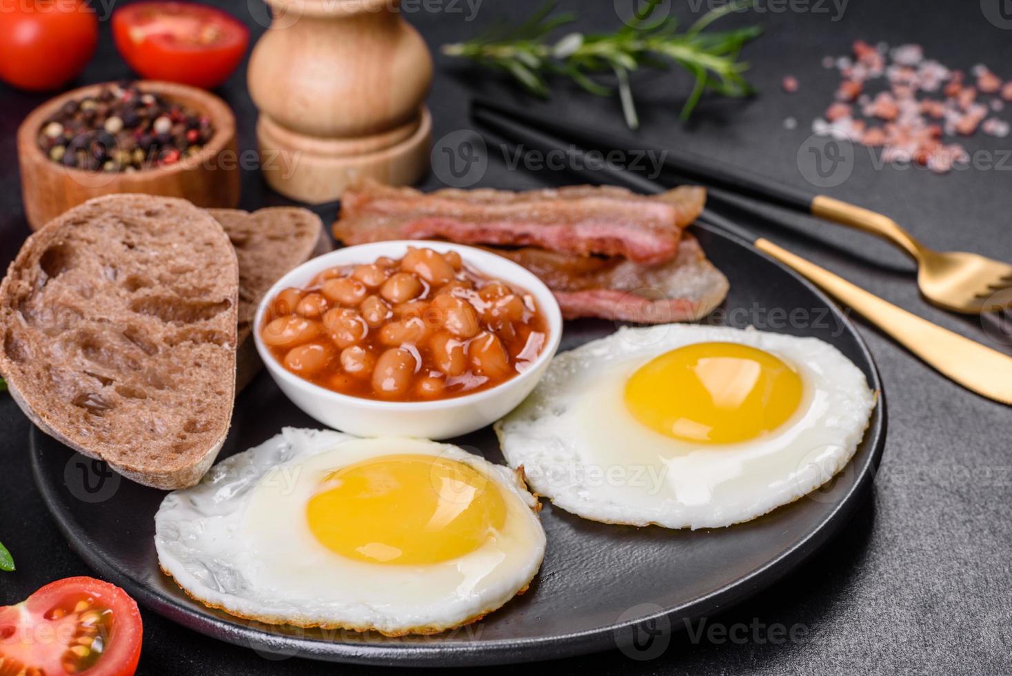 English breakfast with fried eggs, bacon, beans, tomatoes, spices and herbs photo