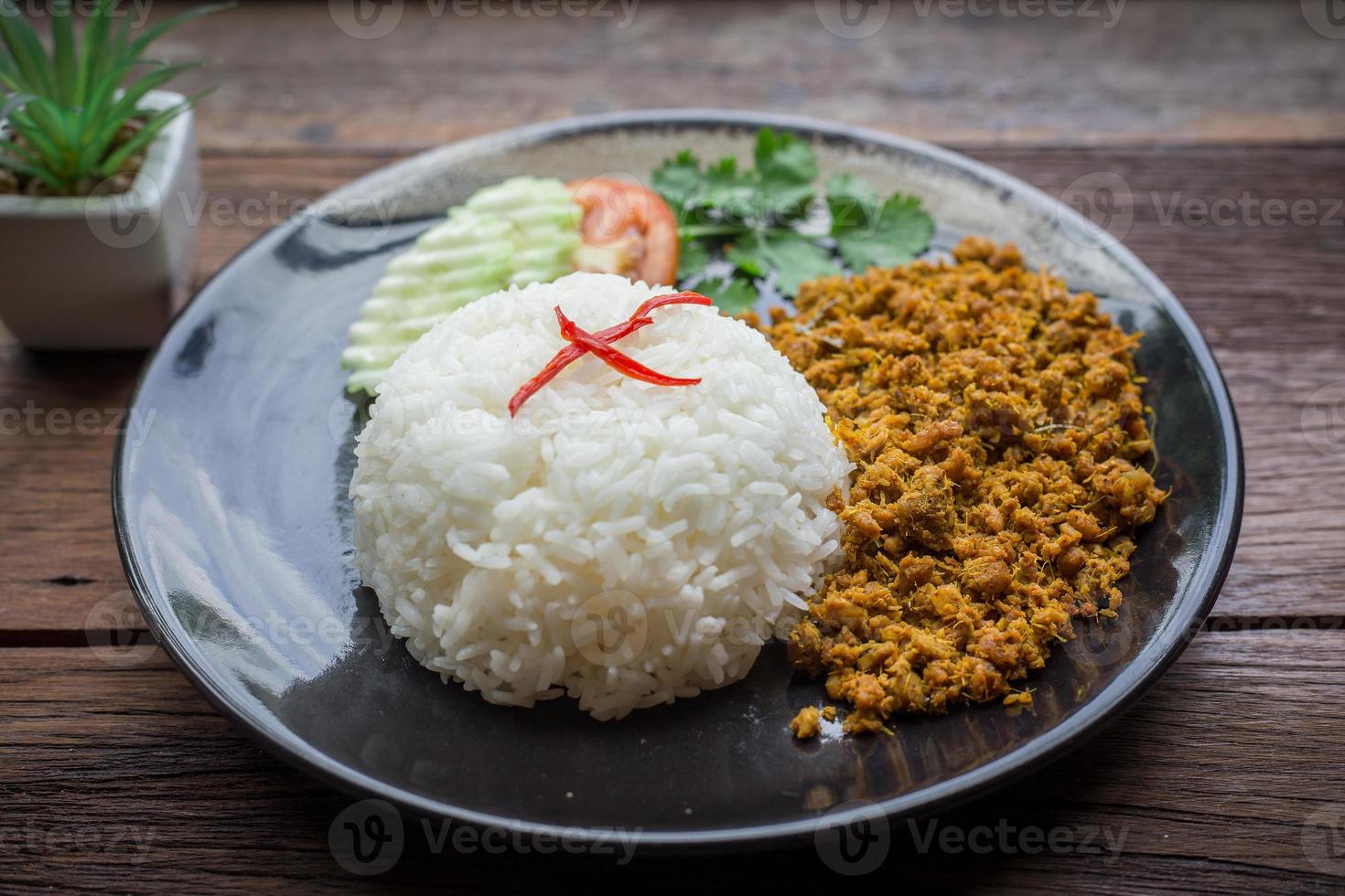 Stir fried pork with yellow curry paste over rice is on a black plate photo