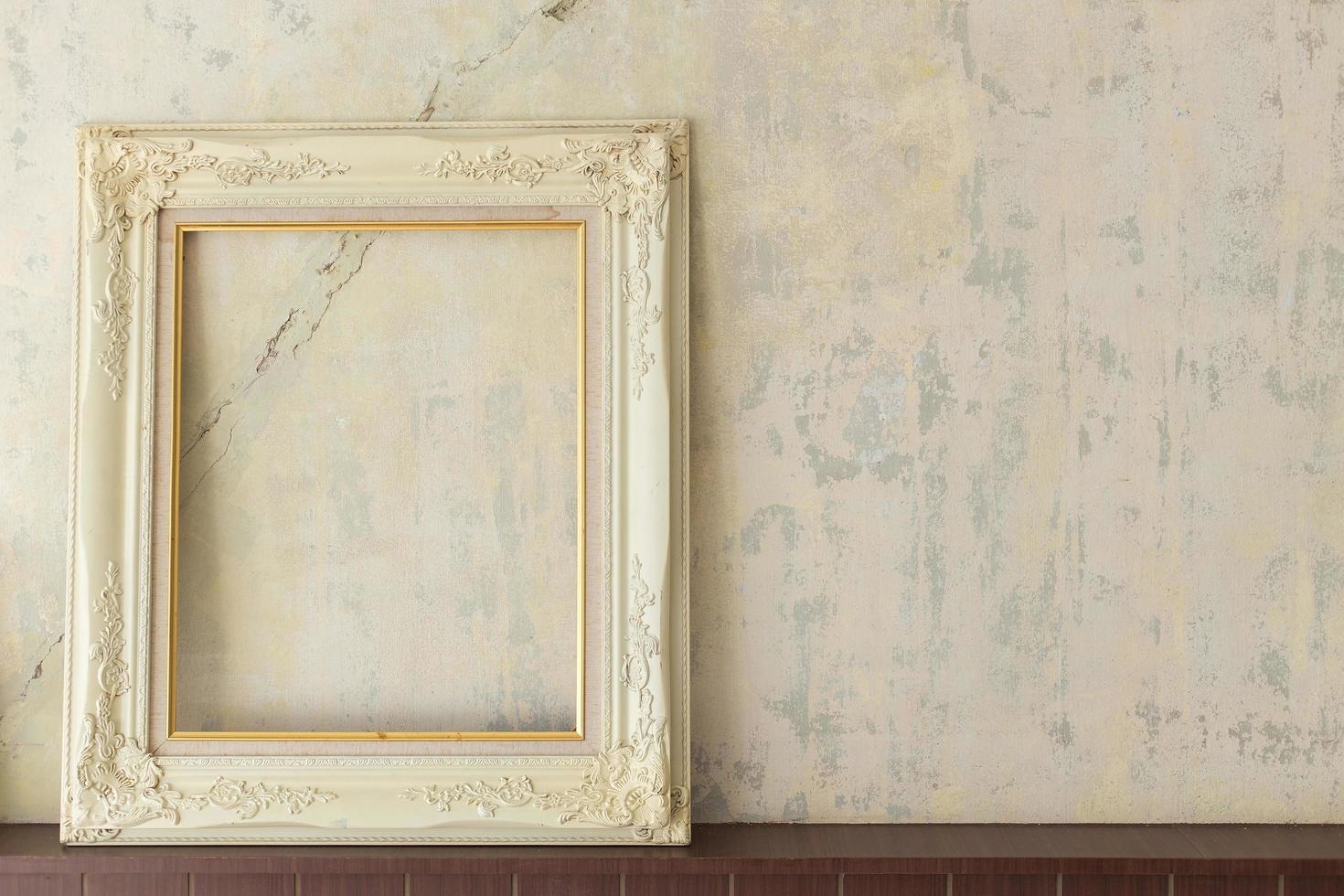An old white wooden picture frame is placed on an old cracked concrete wall. photo