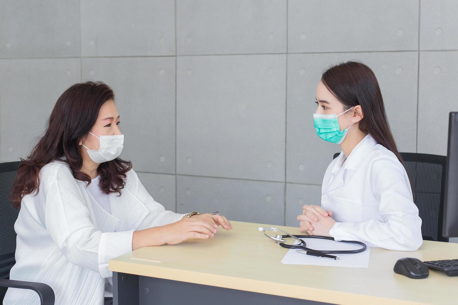 una doctora asiática profesional habla con su paciente mientras usa una mascarilla médica en el hospital en atención médica, contaminación pm2.5, nuevo concepto de protección normal y coronavirus. foto