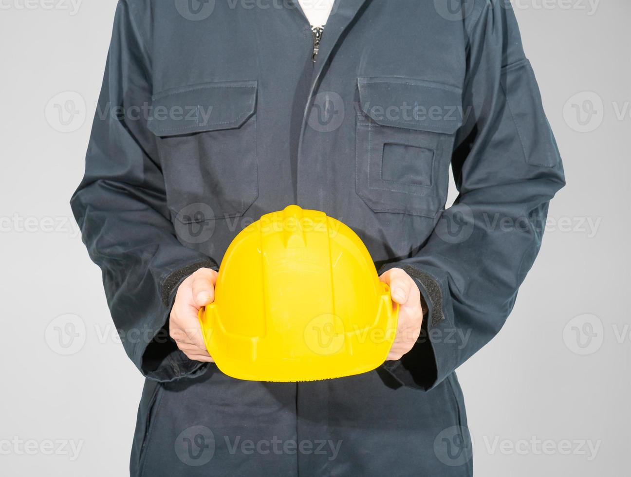 Worker standing in blue coverall holding hardhat photo