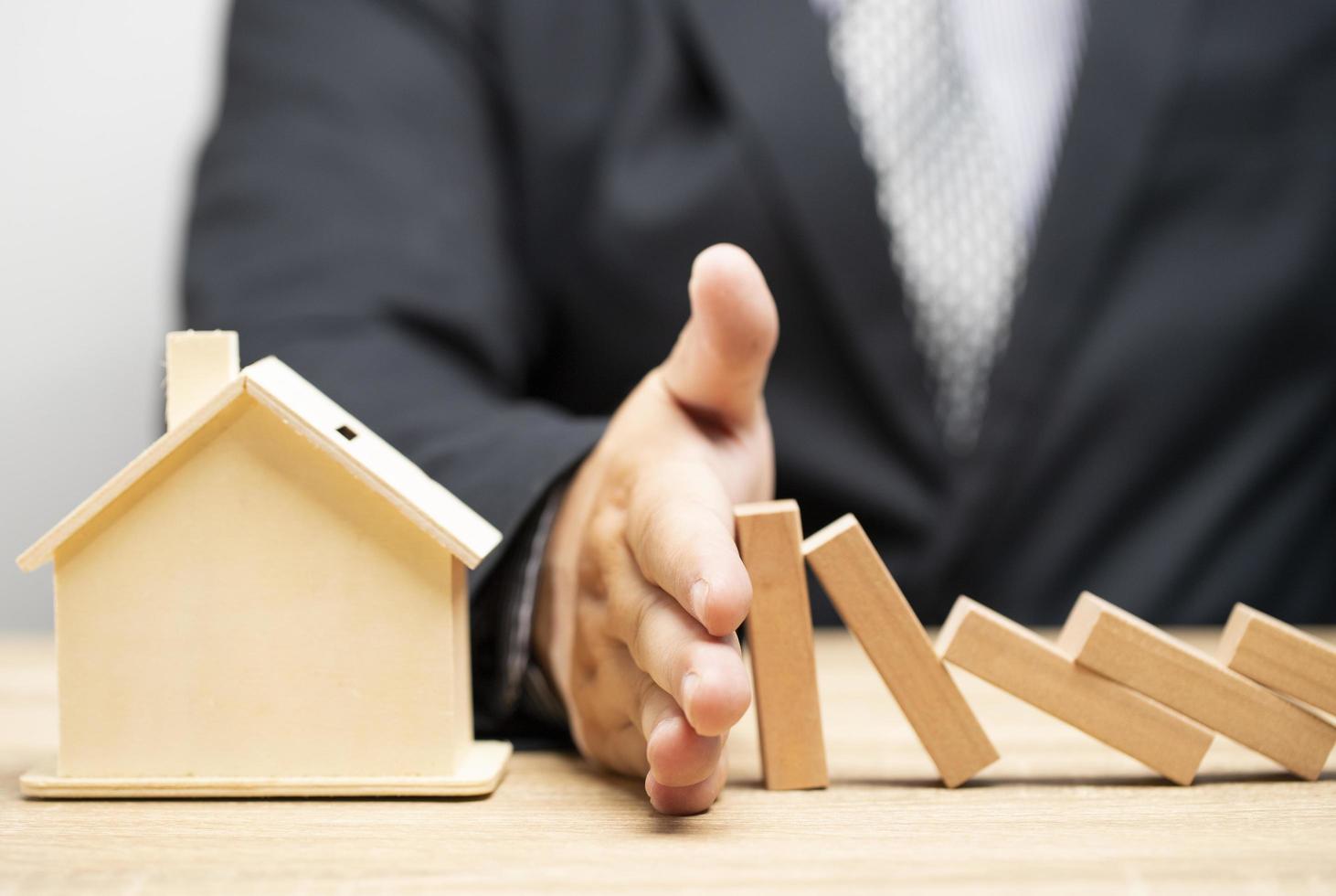 la mano del empresario detiene el riesgo de que los bloques de madera caigan sobre la casa, el seguro del hogar y el concepto de seguridad. foto