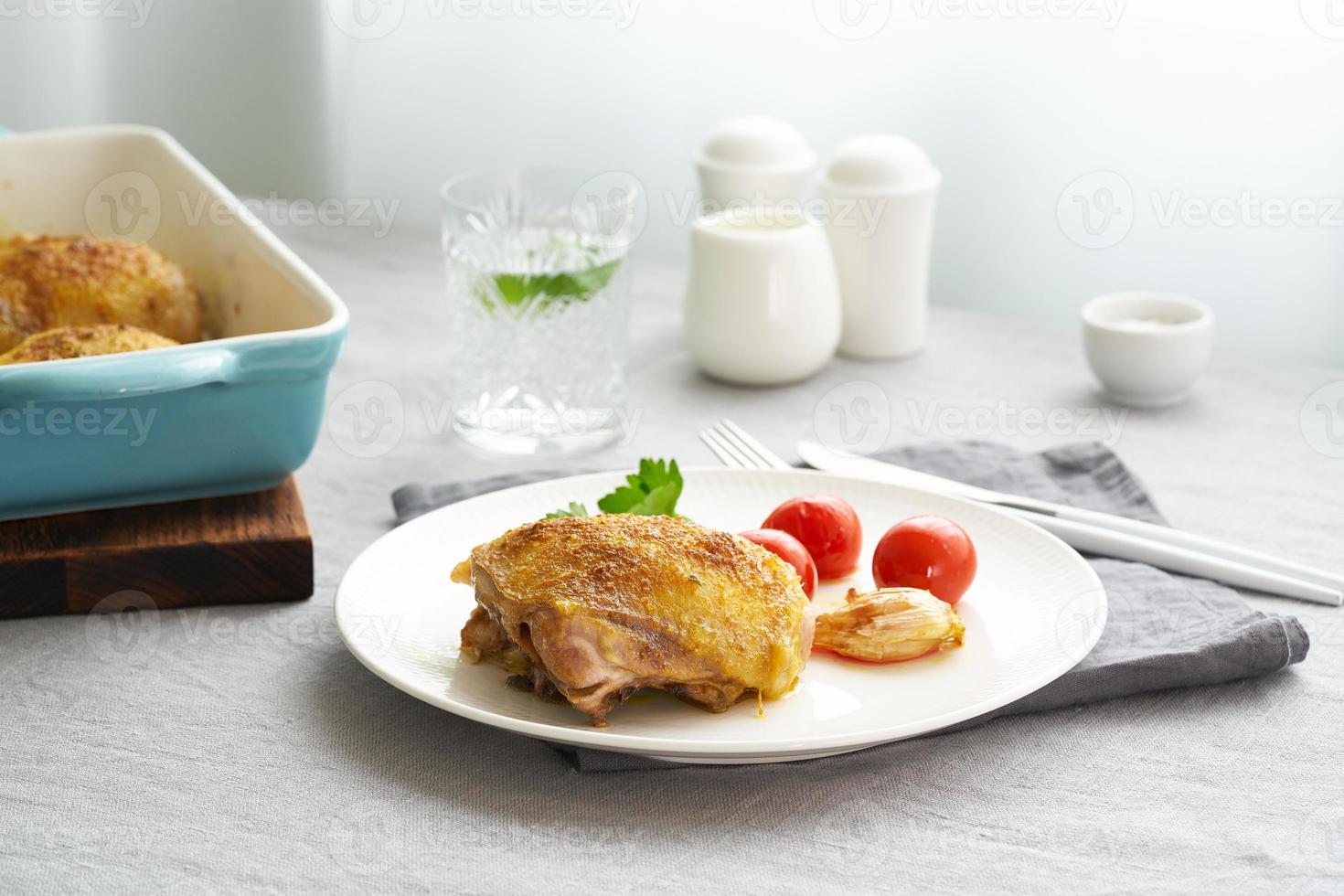 Chicken thighs baked with turmeric, tomatoes and garlic. Fried chicken is on plate photo