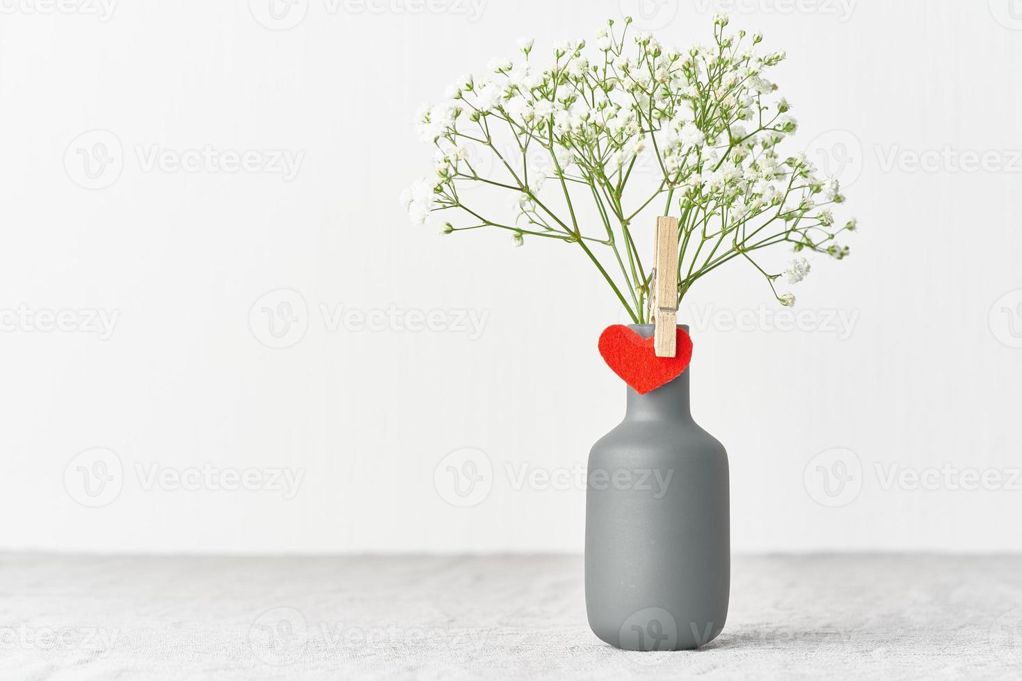 Valentine's Day. Delicate white flowers in a vase. Red felt heart - symbol of lovers. photo