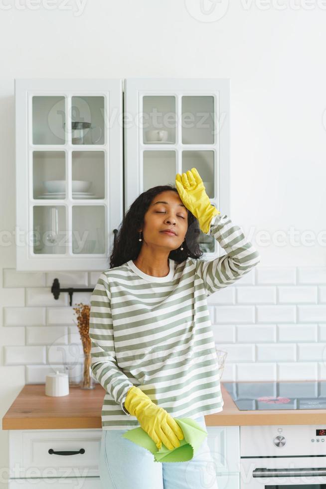 mujer afroamericana sintiendo alivio después de terminar de limpiar la cocina. cansado de las tareas del hogar foto