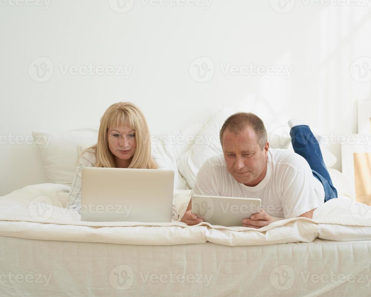 mature couple with digital addiction at home. Man with tablet and woman with laptop photo