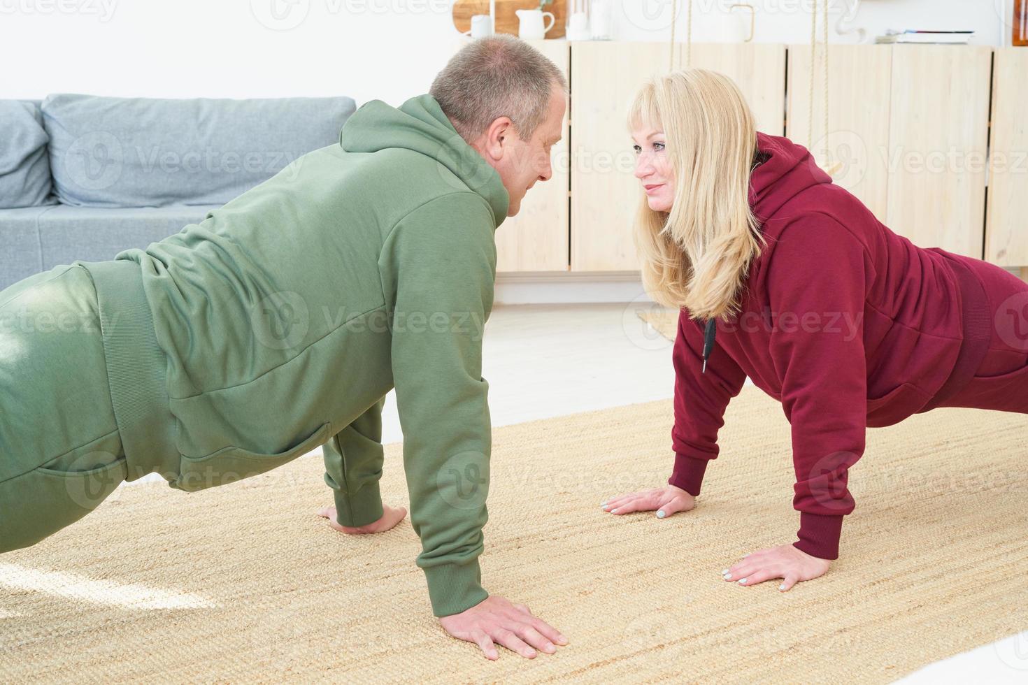 pareja madura activa haciendo ejercicio de tabla y mirándose en la sala de estar en casa. foto