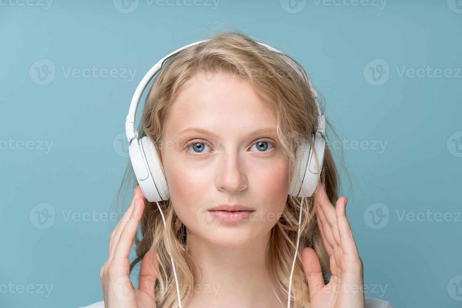 retrato de primer plano de una joven con los ojos cerrados escuchando música a través de auriculares en tono neutro de color foto