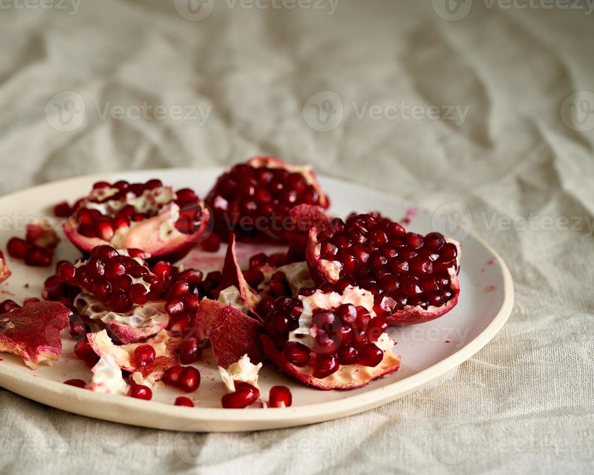 Still life with broken open pomegranate and seeds on plate on table covered with crumpled beige tablecloth photo