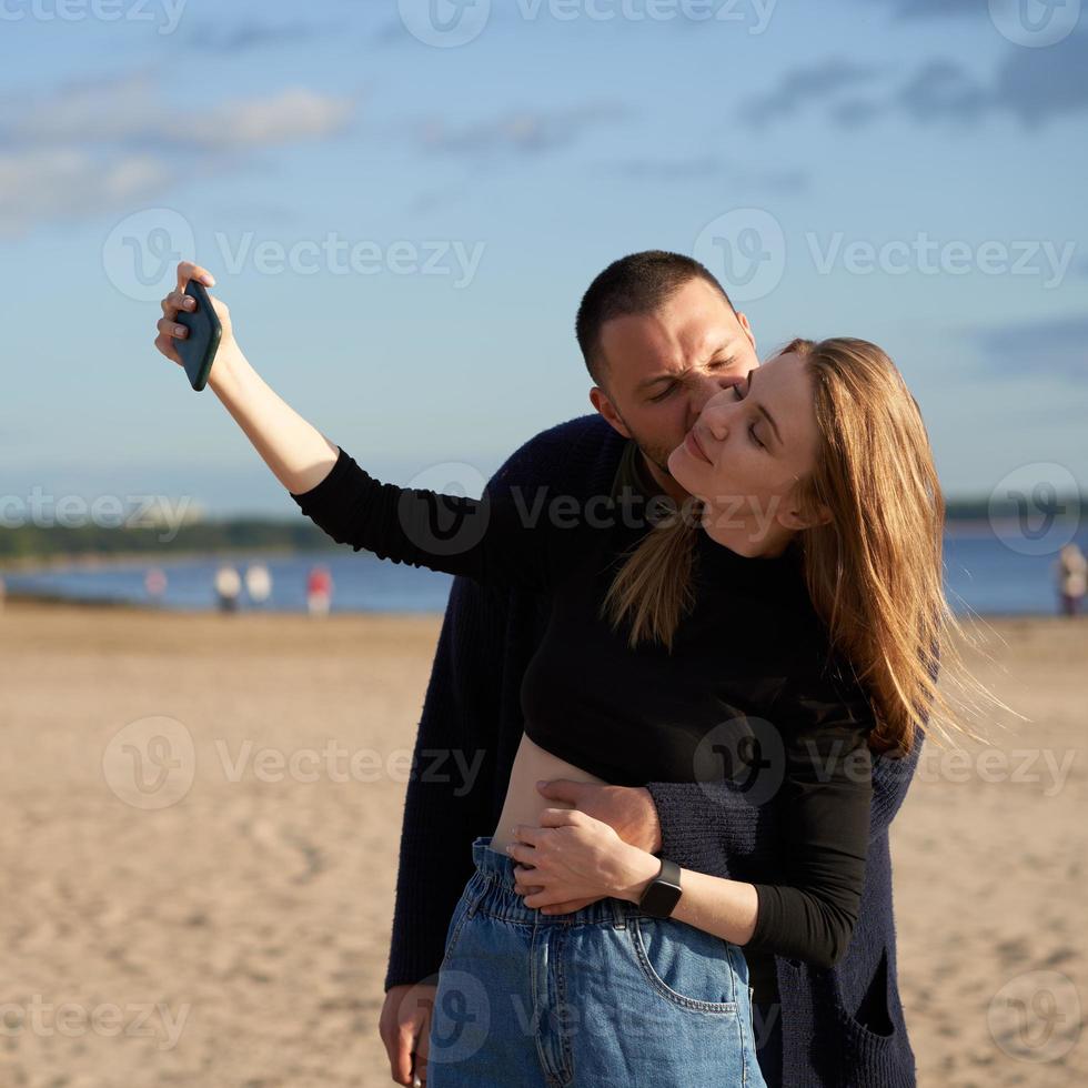 Couple having fun and taking selfie photo on mobile phone on sandy beach in summer or autumn.