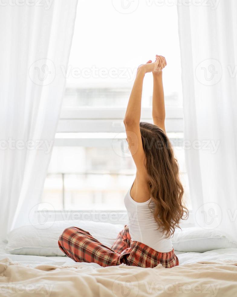 vista trasera de la mujer estirándose en la cama después de despertarse, entrando en un nuevo día, vertical foto