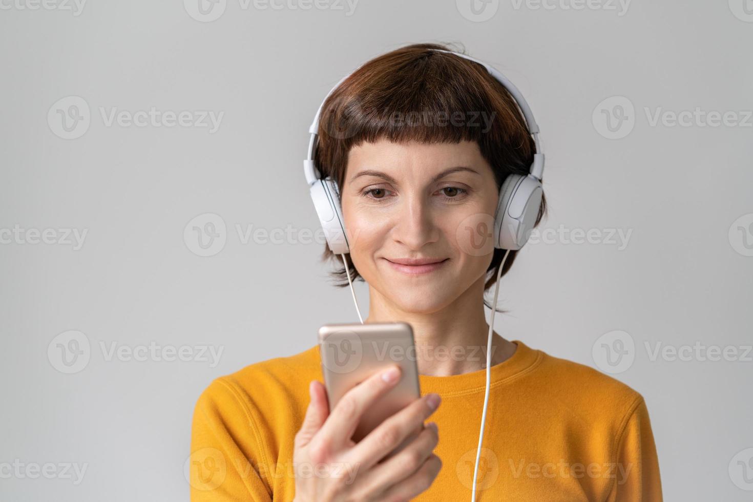 Middle-aged happy woman looking at phone, listening to music. Mature female. photo