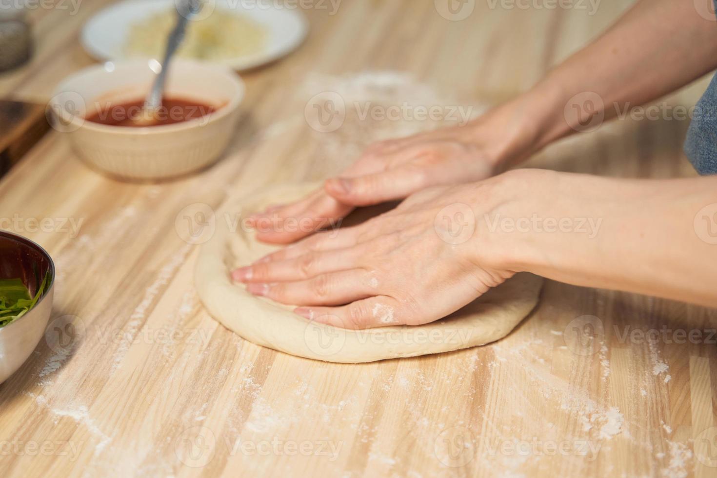 Faceless woman kneading dough on kitchen table at home, apartment. Homemade food photo