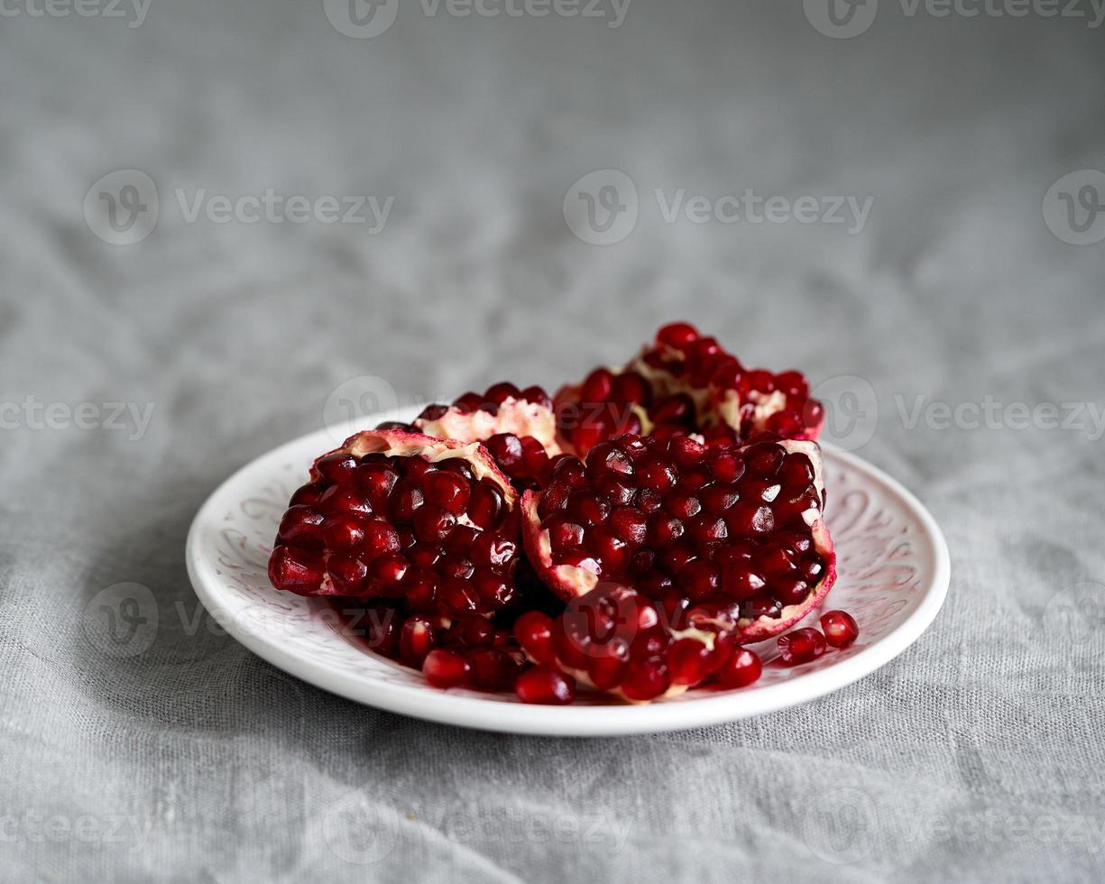 Still life with broken open pomegranate and seeds on plate on table covered with crumpled gray tablecloth photo