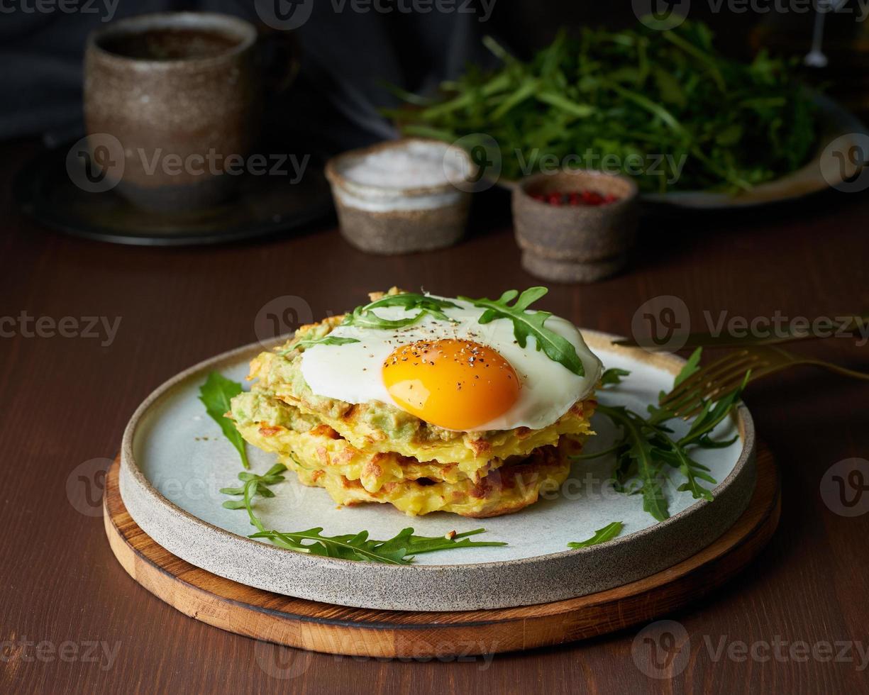 gofres de patata con huevo frito, rúcula y salsa de aguacate. abundante desayuno gordo. mesa marrón oscuro. foto