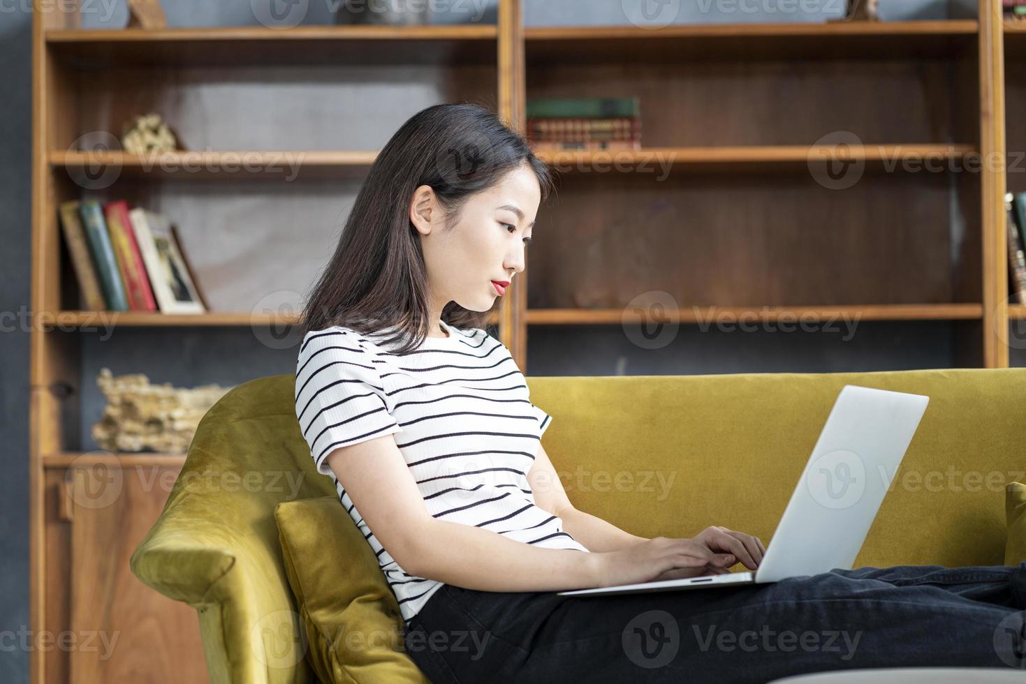 hermosa mujer independiente japonesa sonriendo y escribiendo en la computadora en el hotel en el sofá foto