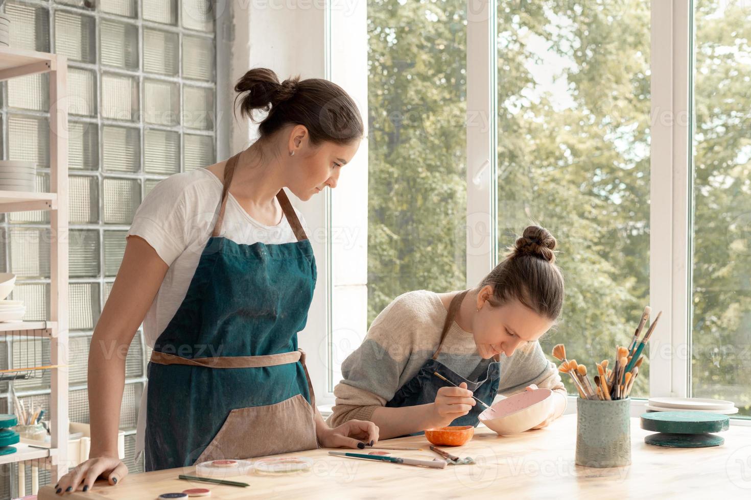 mujer haciendo cerámica. atractiva joven calificada en delantal de pie en la mesa y enseñando foto