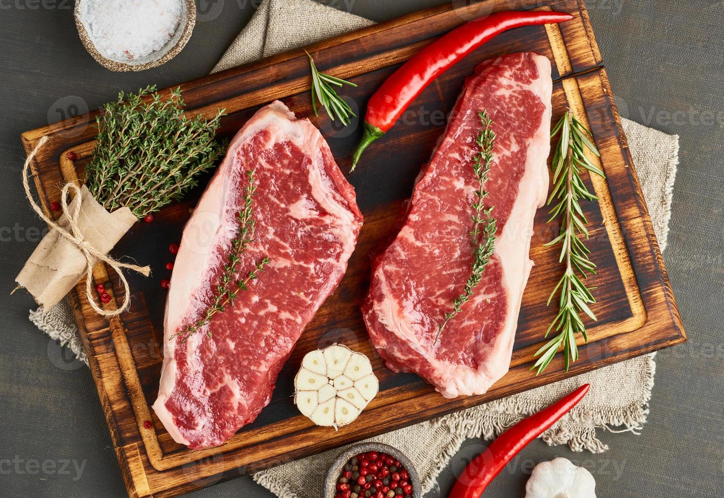 Seasoning raw steak with salt, thyme, garlic. Two big whole piece of raw beef meat photo