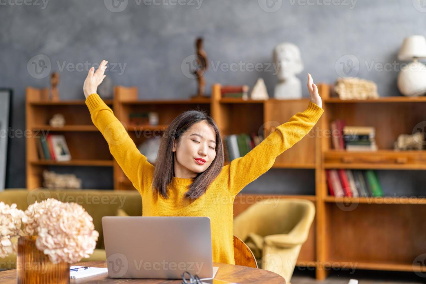 mujer asiática trabajando en una laptop en casa o en un café estirándose cansadamente foto